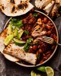 Mexican Chipotle Pork and Beans with tortillas, avocado and limes connected  the side