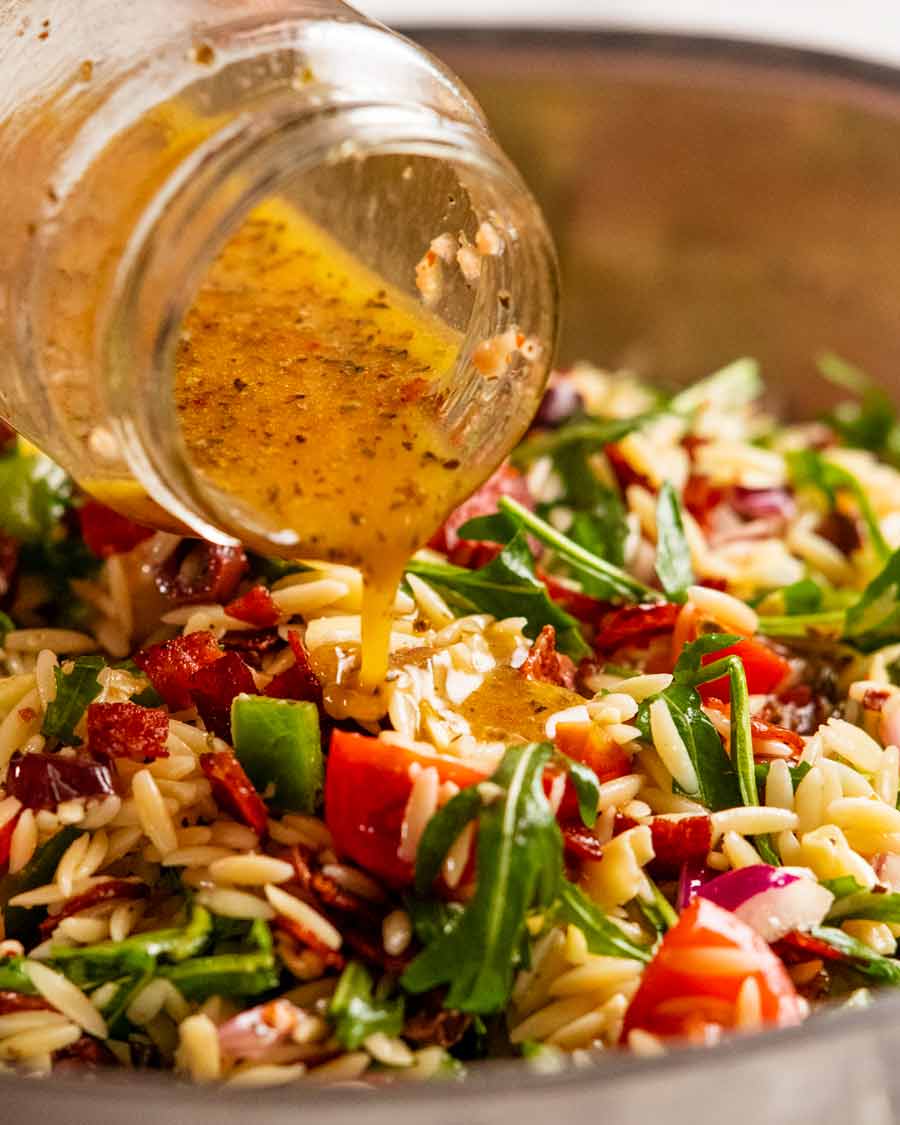 Pouring dressing over Italian risoni/ orzo salad with crispy salami bits